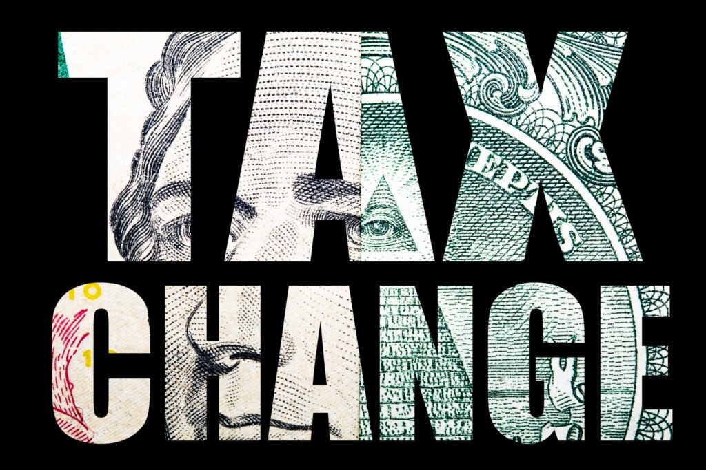 The words "TAX CHANGE" are written in bold capital letters with a background of a close-up image of U.S. currency.