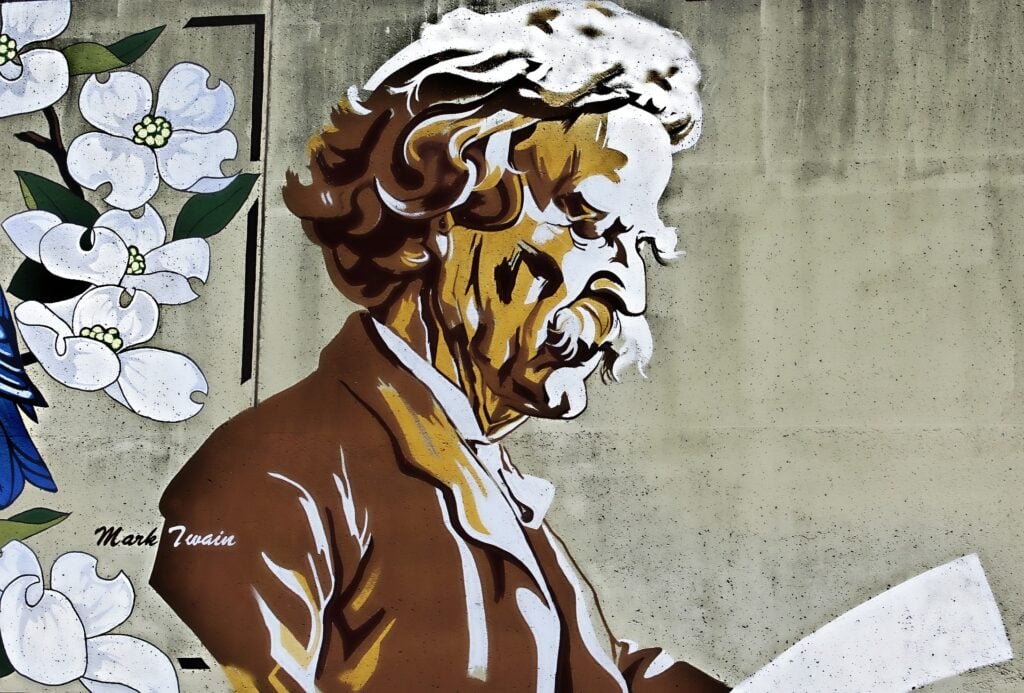 Wall mural depicting an older man reading, with an adjacent floral design. The name "Mark Twain" is visible in the lower left corner.