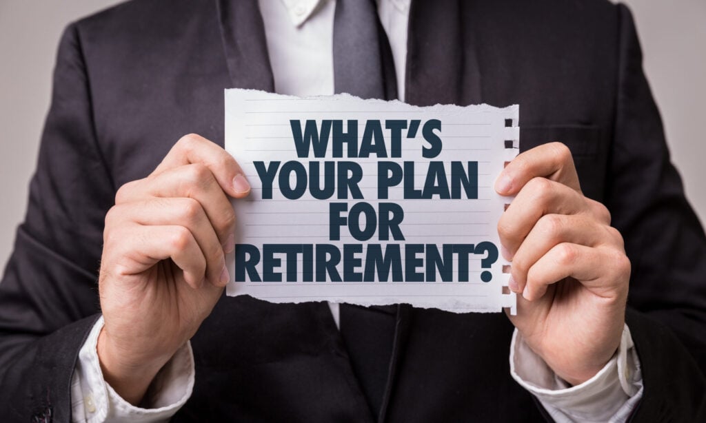 A person in a suit holds a torn piece of paper with the words "What’s your plan for retirement?" written on it.