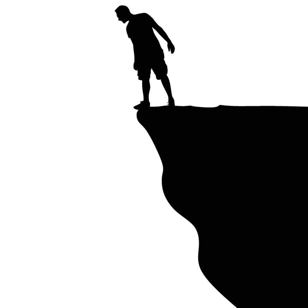 Silhouette of a person standing and peering over the edge of a steep cliff.
