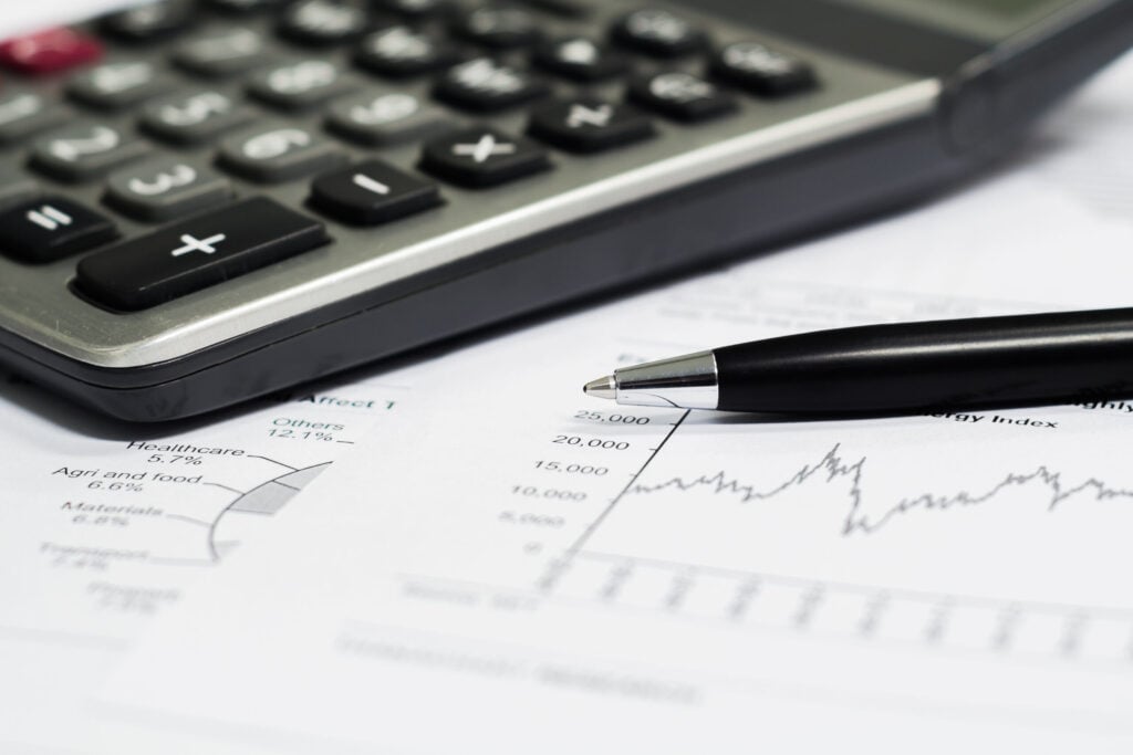 Close-up of a calculator and pen on top of financial charts and documents with graphs and data.