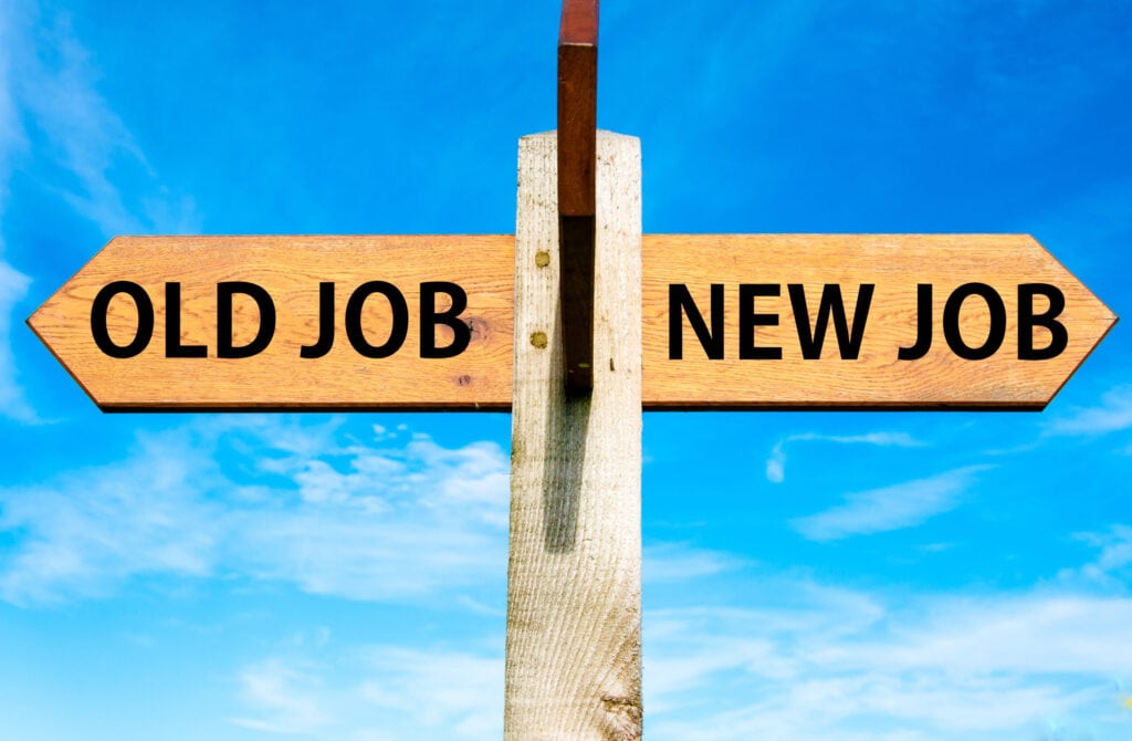 A wooden signpost with two arrows pointing in opposite directions against a blue sky; one arrow is labeled "Old Job," and the other is labeled "New Job.