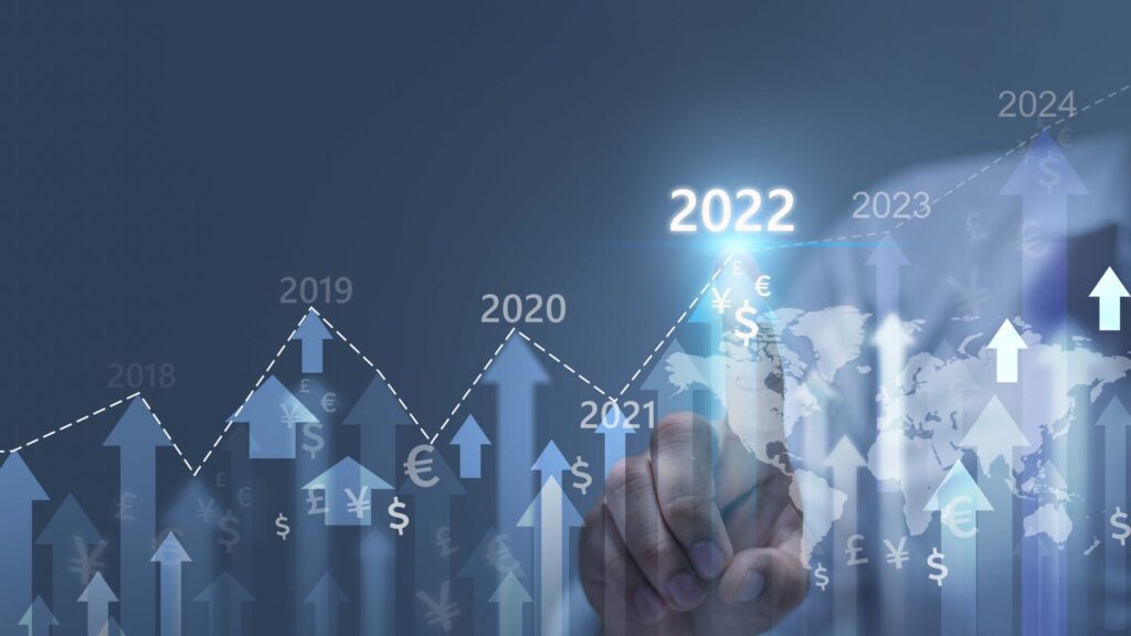 A hand points to "2022" on a rising financial graph with global currency symbols and an upward trend indicating growth from 2019 to 2023.