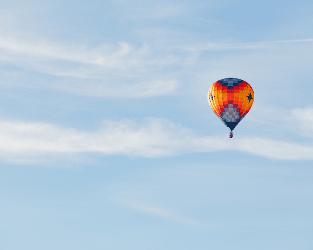 A colorful hot air balloon with a checkered pattern floats against a clear blue sky with wispy clouds.