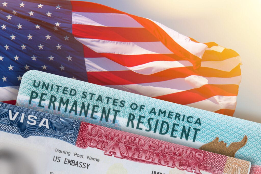 A United States permanent resident card and visa are displayed in front of an American flag.