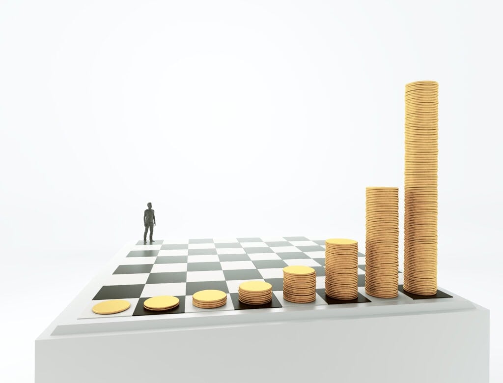 A person stands in the distance on a large, white chessboard, with stacks of coins increasing in height along one side.