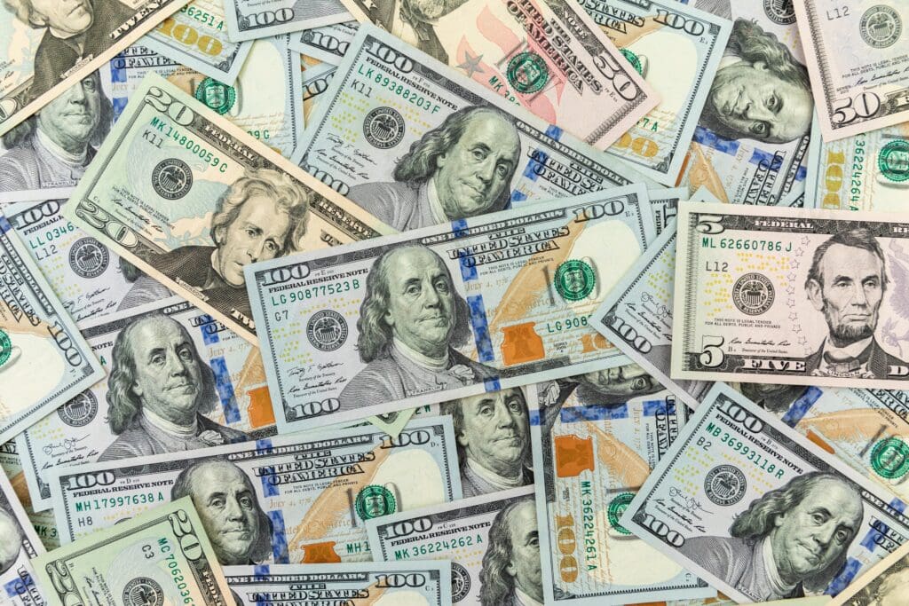 A scattered assortment of American currency bills in various denominations, including $100, $50, $20, and $5 notes.