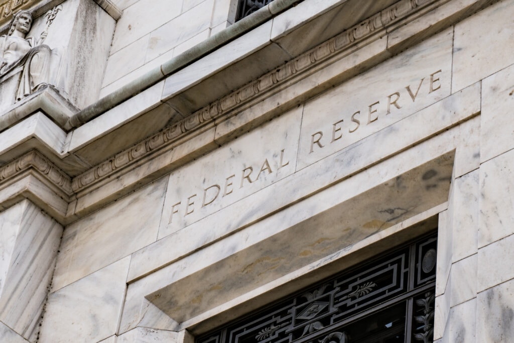 The facade of a building with "Federal Reserve" engraved on its wall. The structure is made of light-colored stone with decorative elements.