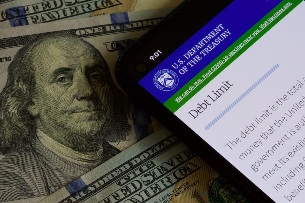 A smartphone displaying the U.S. Department of the Treasury website with the "Debt Limit" section open, against a background of hundred-dollar bills.