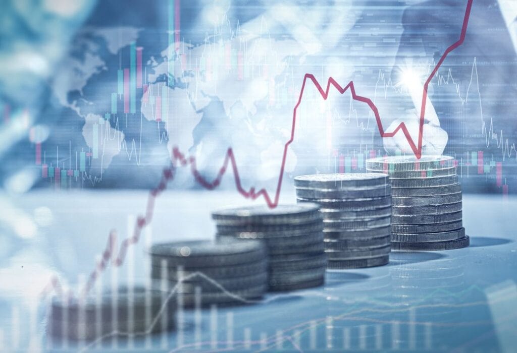A series of coin stacks in the foreground with a red financial graph line and world map overlaid, indicating economic trends or financial data analysis.