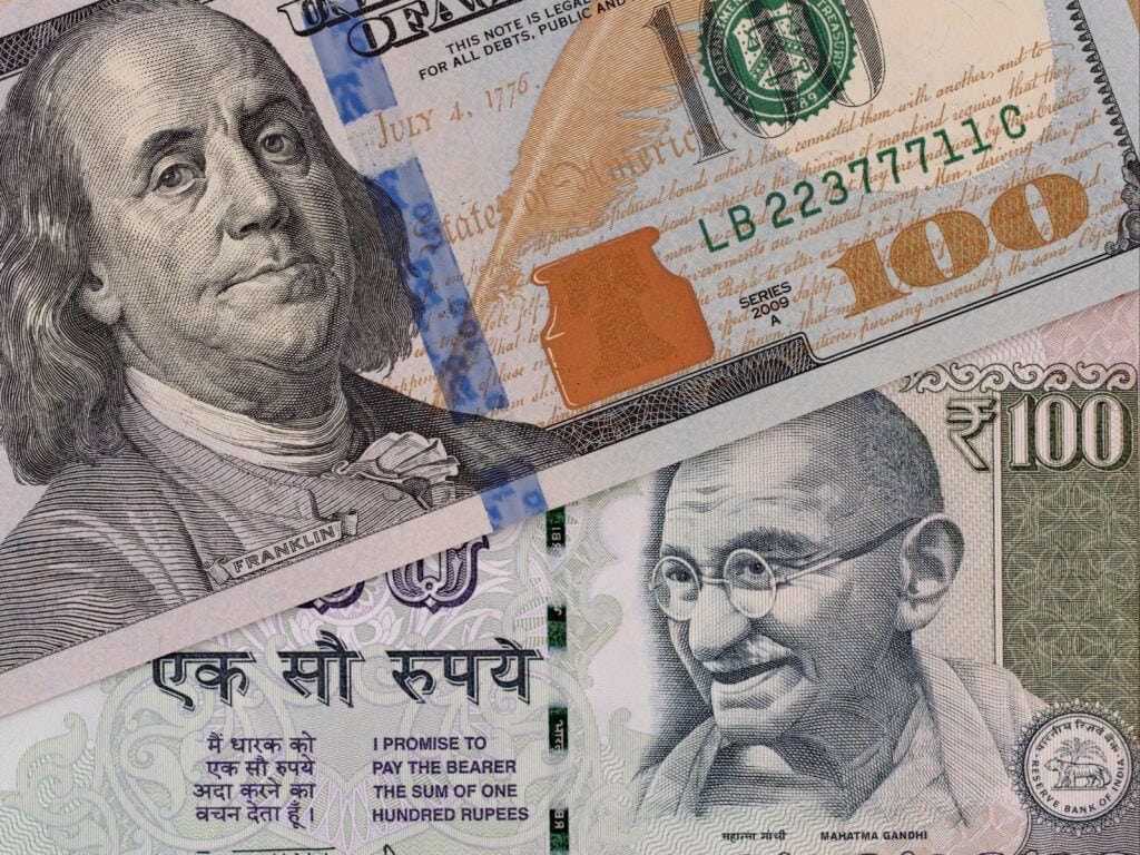 A close-up of a US 100 dollar bill featuring Benjamin Franklin and an Indian 100 rupee note featuring Mahatma Gandhi placed side by side.