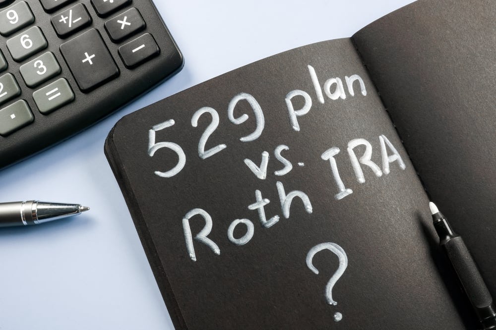 A notebook with "529 plan vs. Roth IRA?" written on a black page, next to a pen and calculator, suggesting a comparison of savings options.
