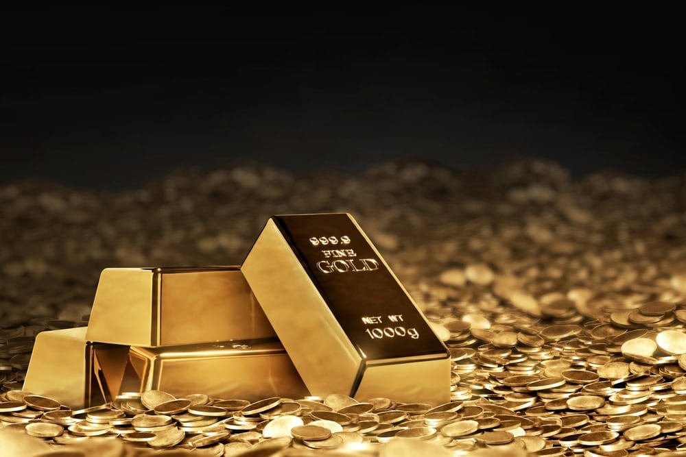 Several gold bars and numerous gold coins scattered on a reflective surface with a dark background.