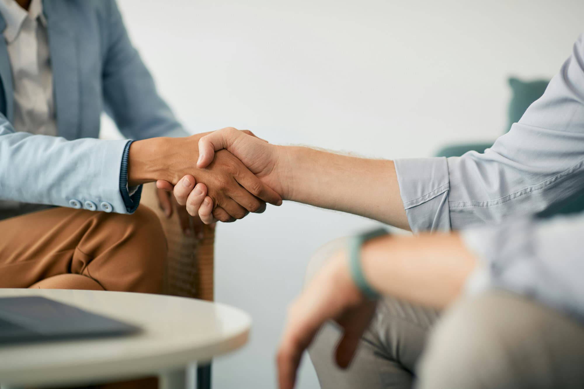 Two people sitting and shaking hands across a table, suggesting agreement or partnership in a professional setting.