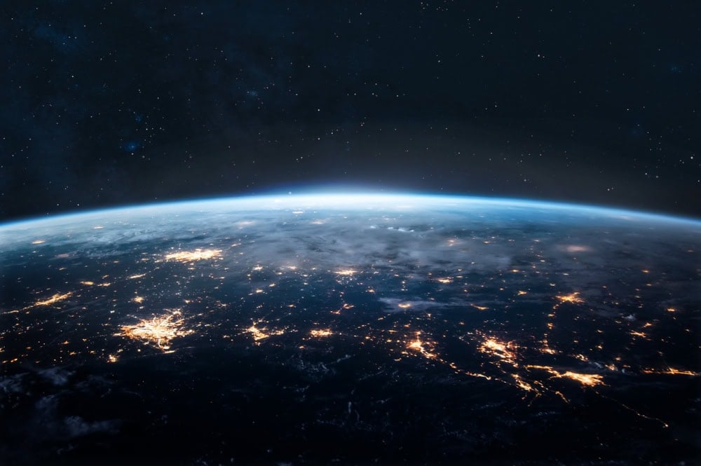 View of Earth from space showing a curved horizon, city lights illuminating the surface, and a faint blue atmosphere against a dark star-filled sky.
